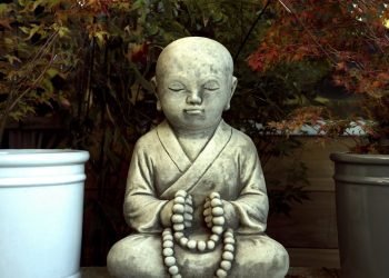 Zen Buddhist statue in tranquil garden with autumn leaves.